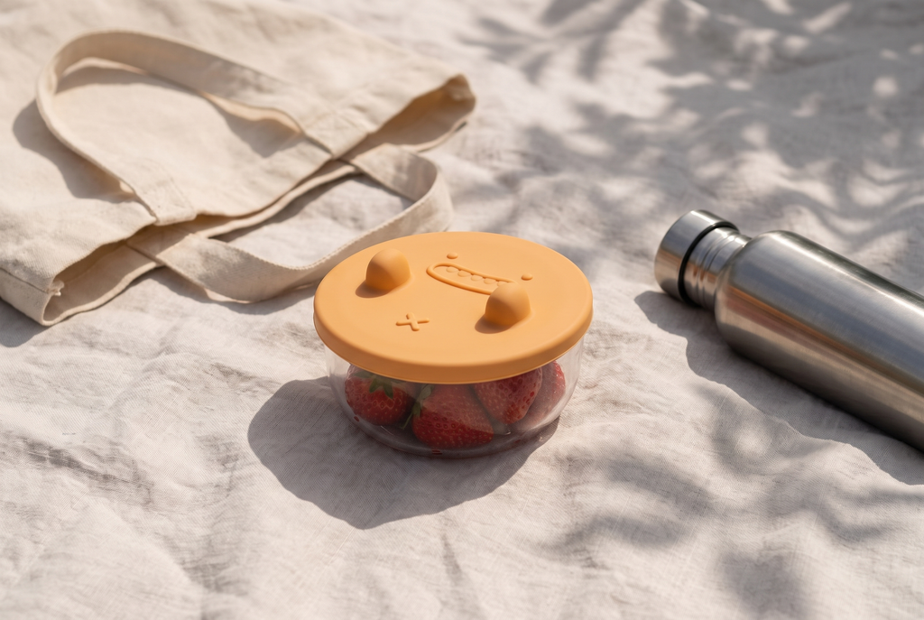 The sealed snack pot of strawberries on a picnic blanket beside a canvas tote
