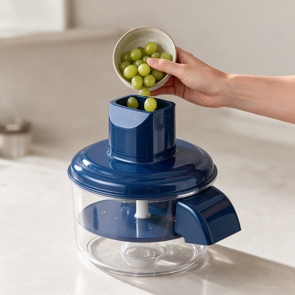 A hand tipping grapes into the top of the peeler